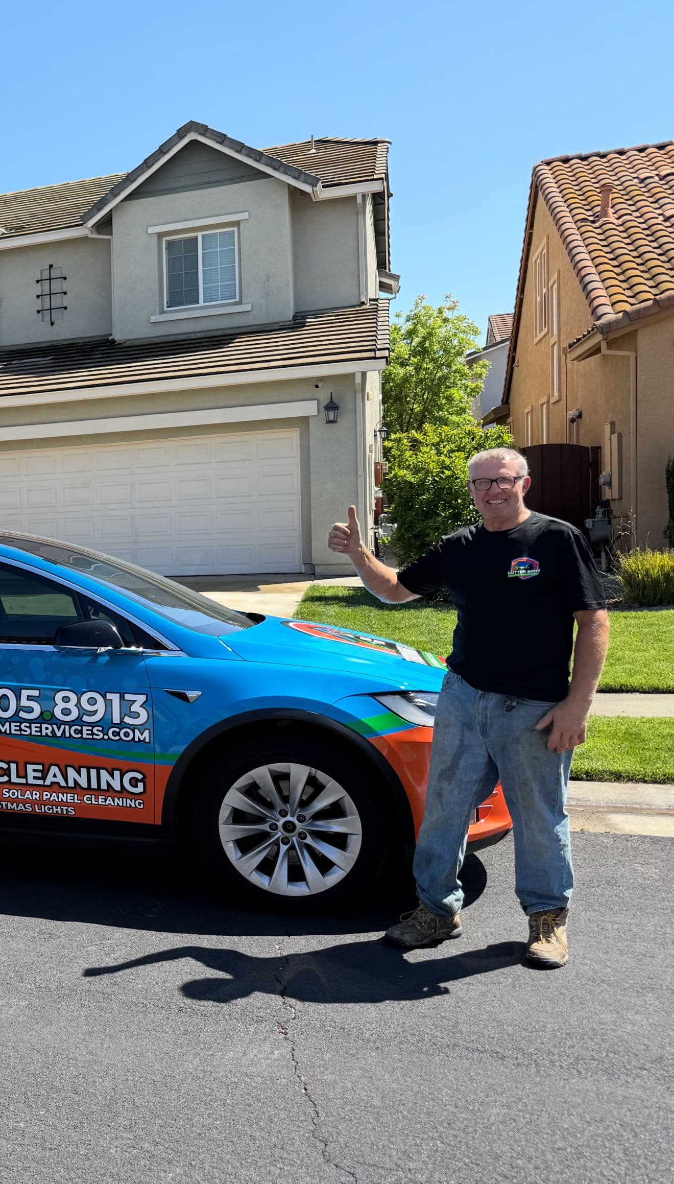 Man giving a thumbs up next to a solar panel cleaning service vehicle in a residential area.